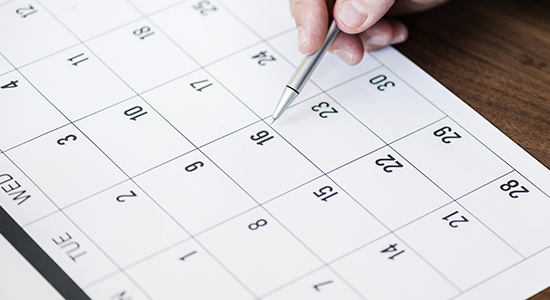 Calendar and a hand holding a pen and pointing at a date