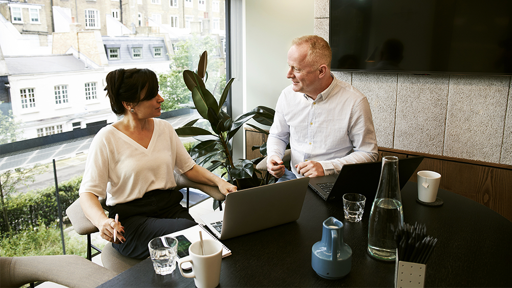 A woman and man sitting at a desk talking.