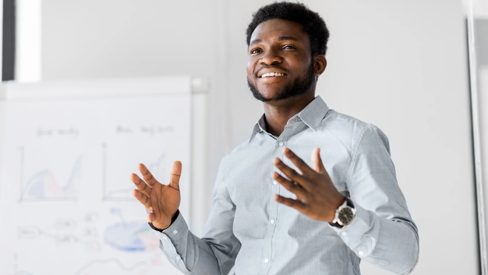 Person presenting with charts behind them. 