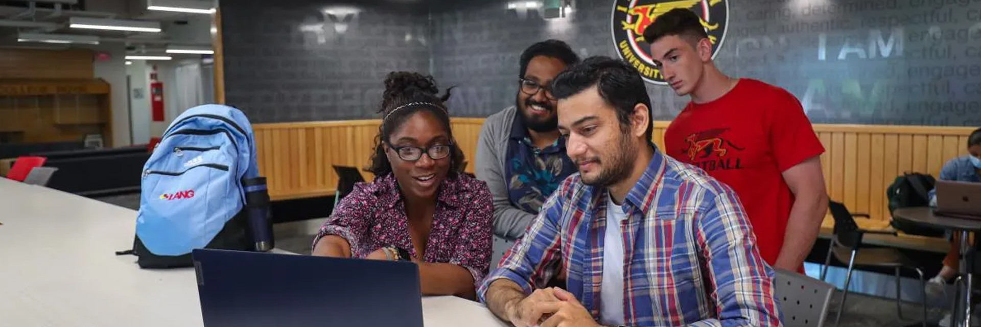 a photo of students point and looking at a laptop 
