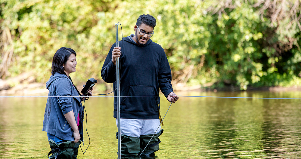 two graduate students outside standing in a pond