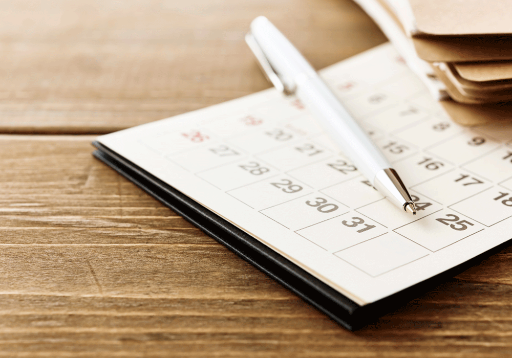 Calendar and pen resting on wood table.