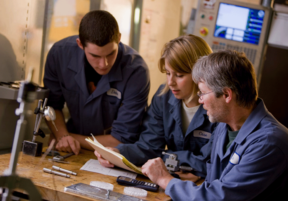Students and instructor reviewing work at a desk in a classroom.
