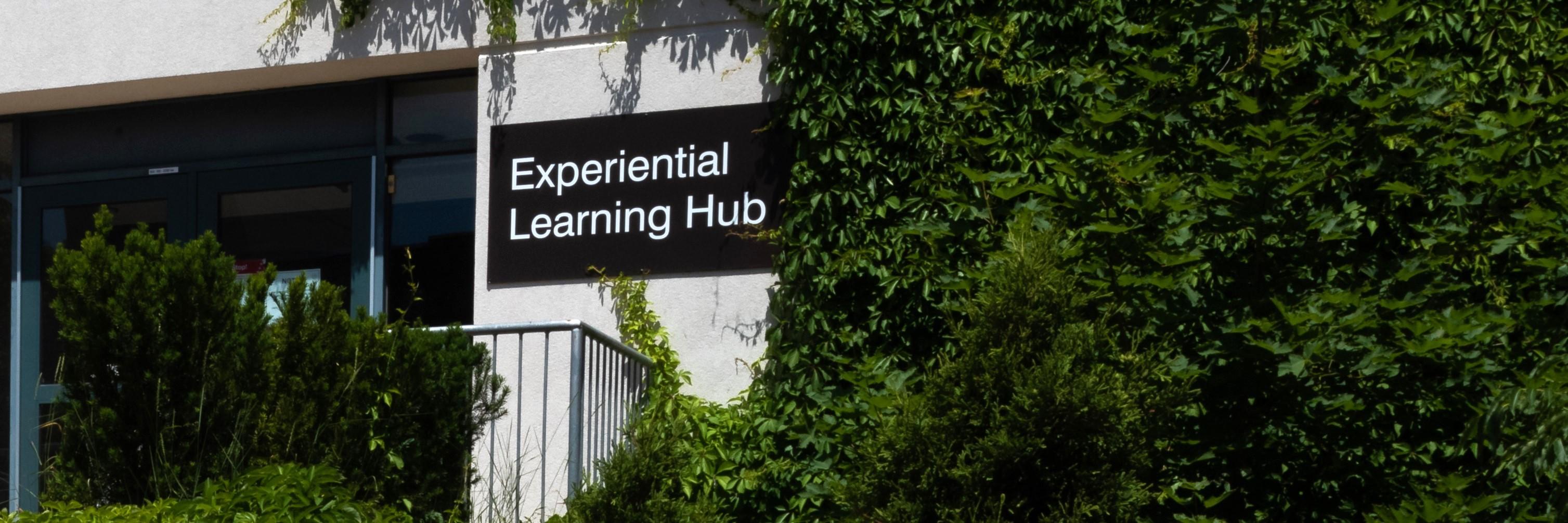 Sign reading "Experiential Learning Hub" on foliage-covered building