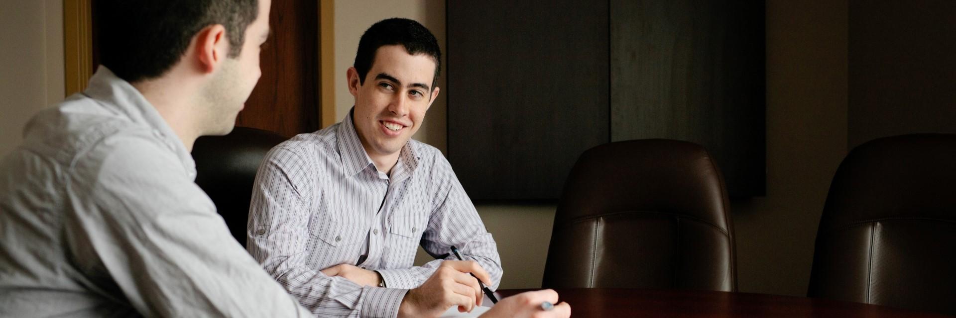 Two people in conversation at a board room table in an office.