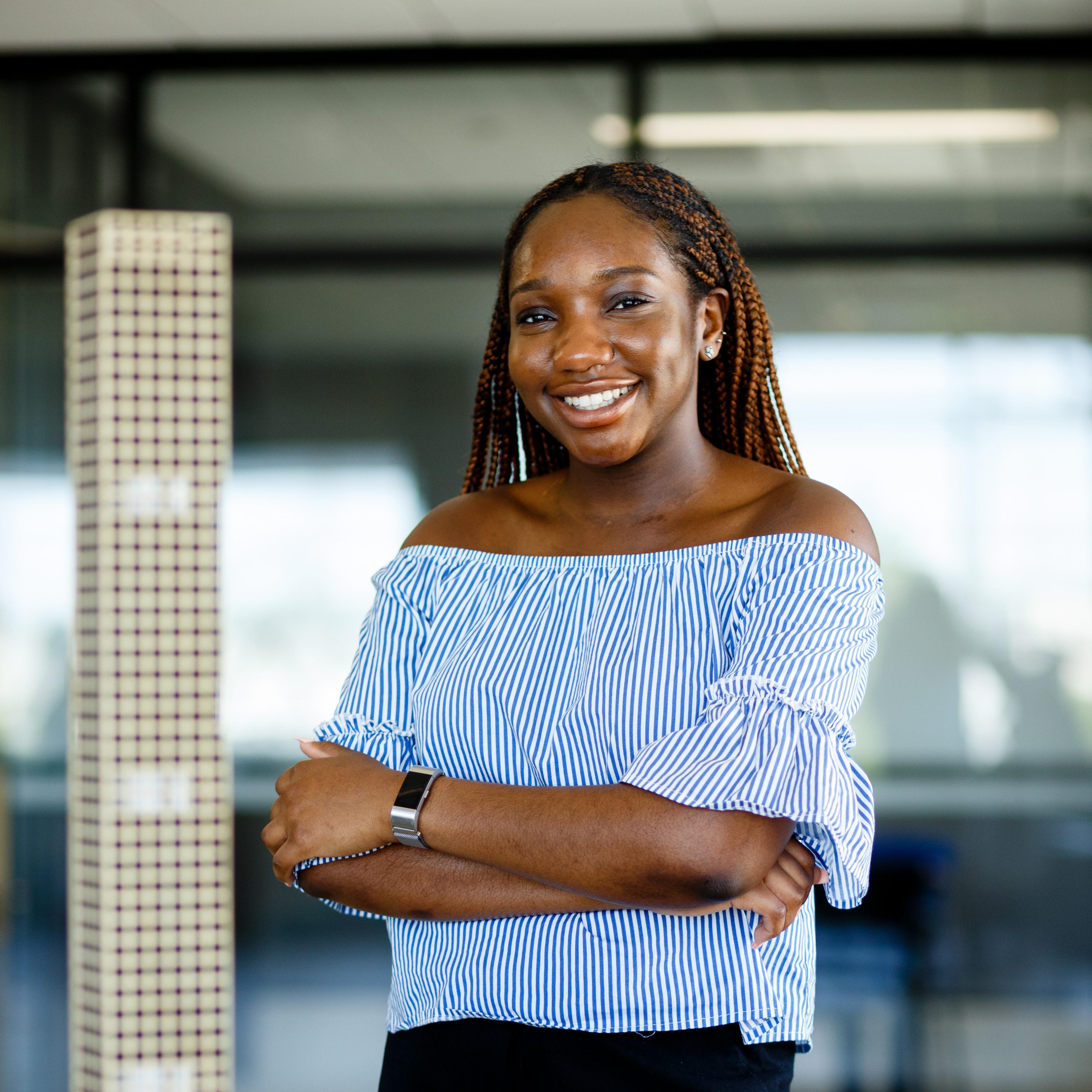 person smiles standing with crossed arms in front of a model skyscraper