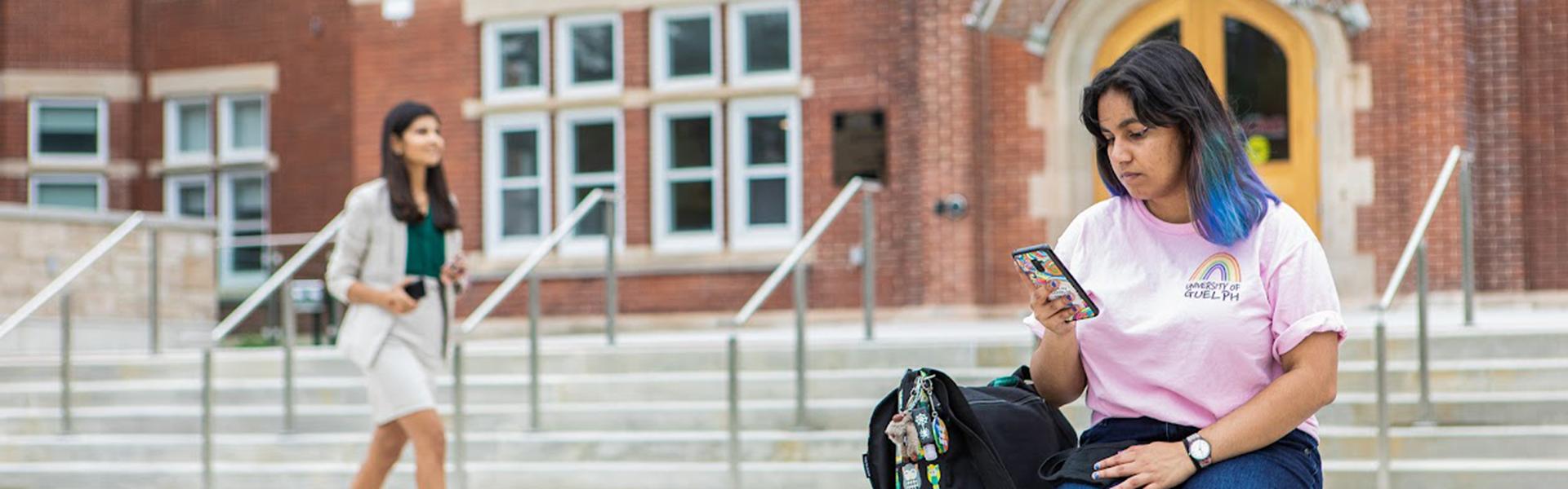 female U of G student sitting and looking at her smartphone