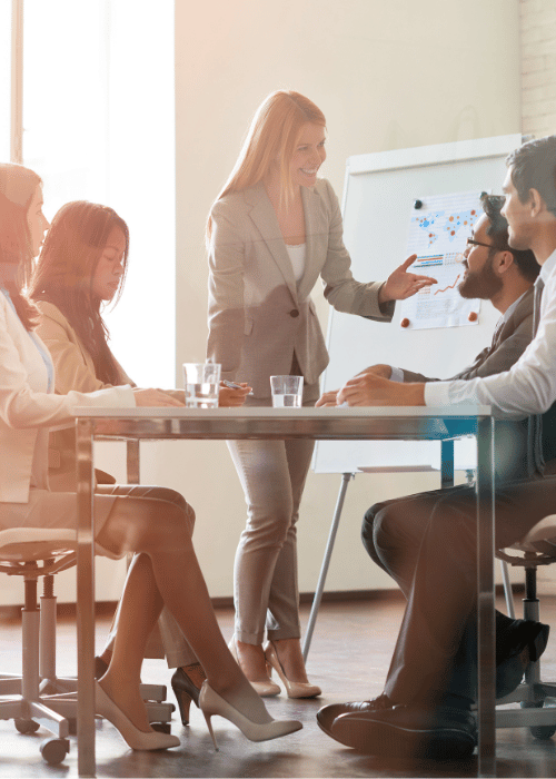 Five people at a table talking with board in background with graphs