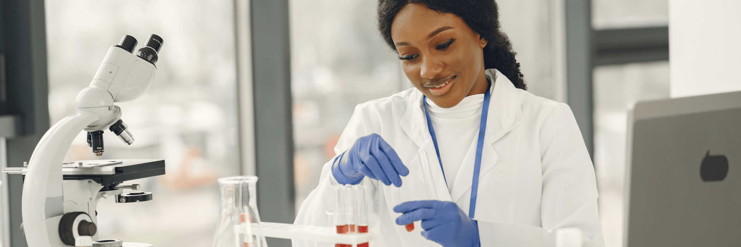 Lab technician working at a desk with a microscope and test tubes