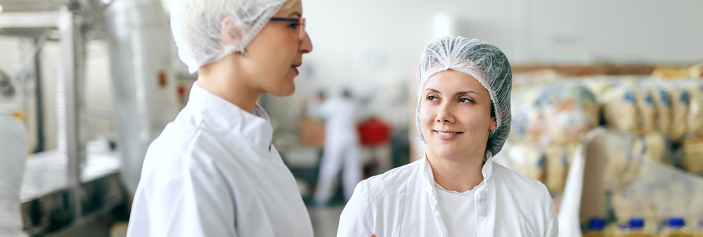 two people in lab coats talking in a food production facility