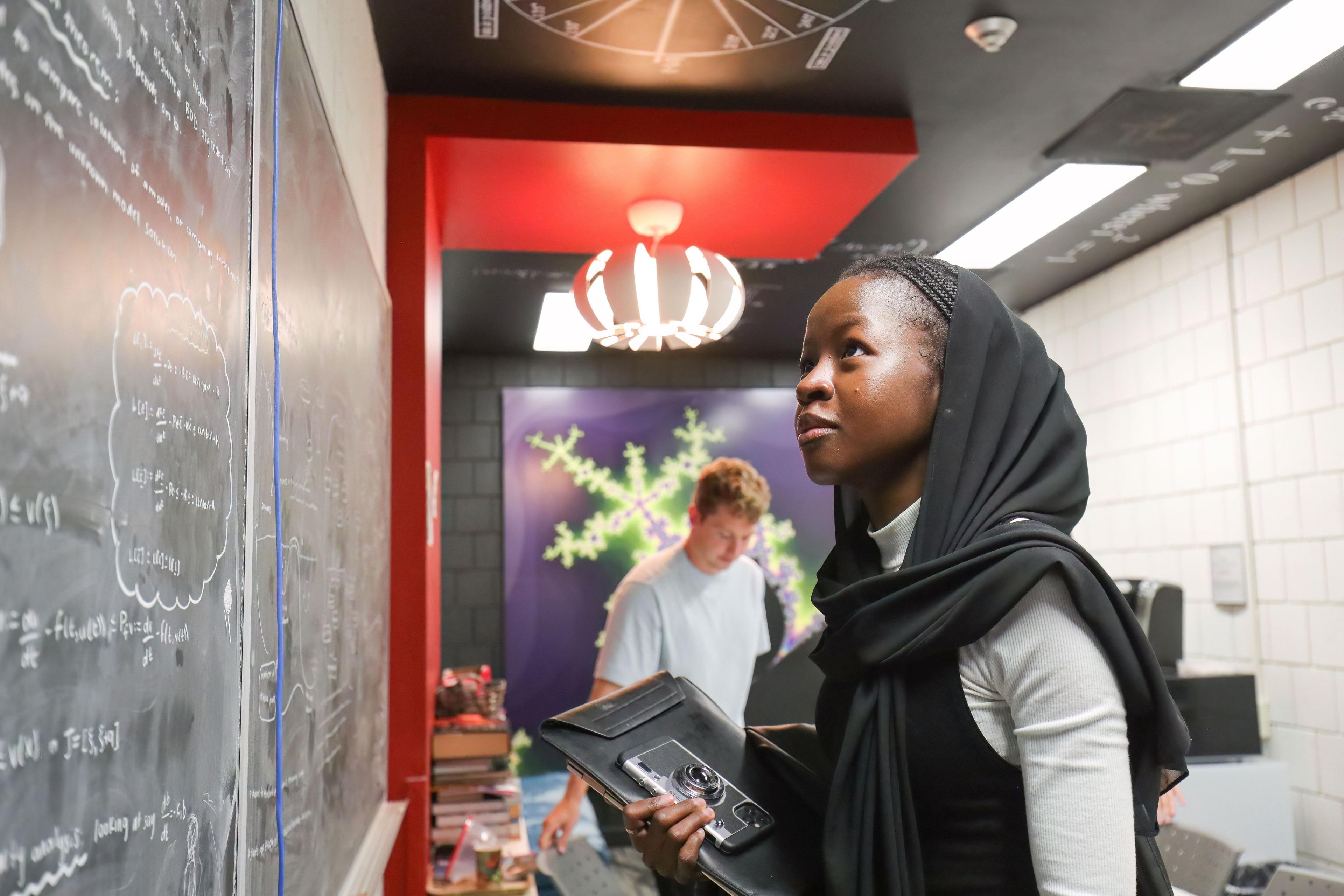 A student looking at a chalk board with mathematical notes written on it.