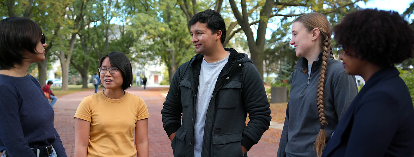 five students on u of g winegard walk, talking to each other with green trees above them