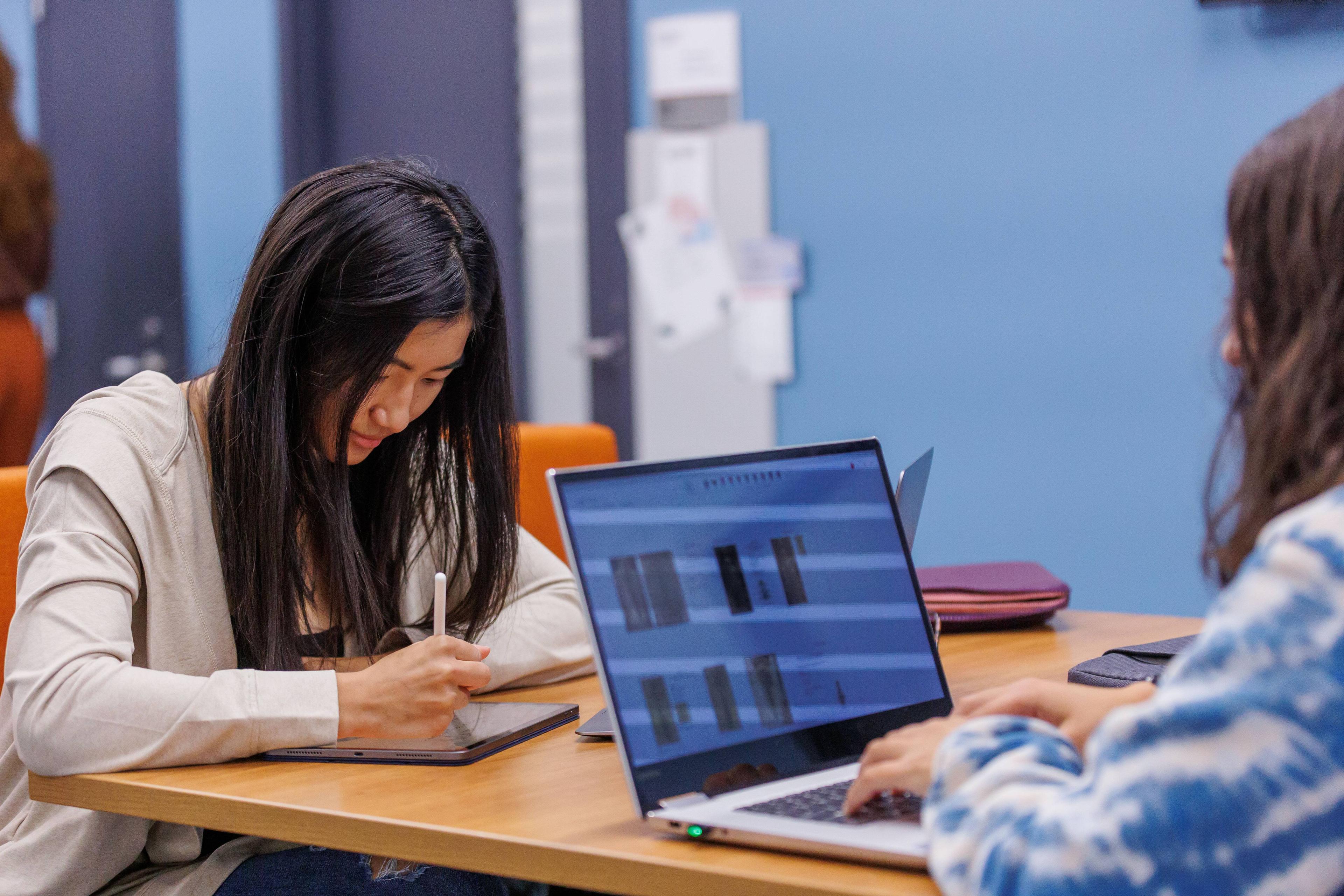 Two students working on their devices at a desk