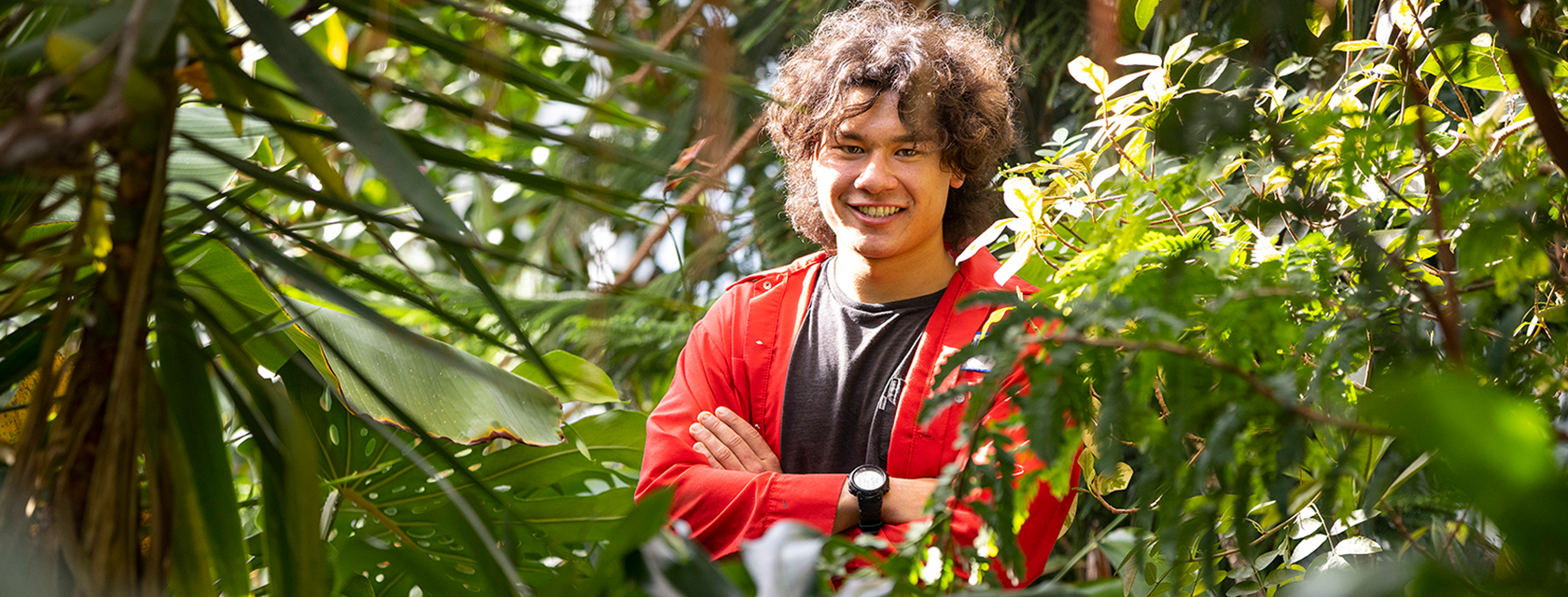 a student in a greenhouse smiling and crossing his arms