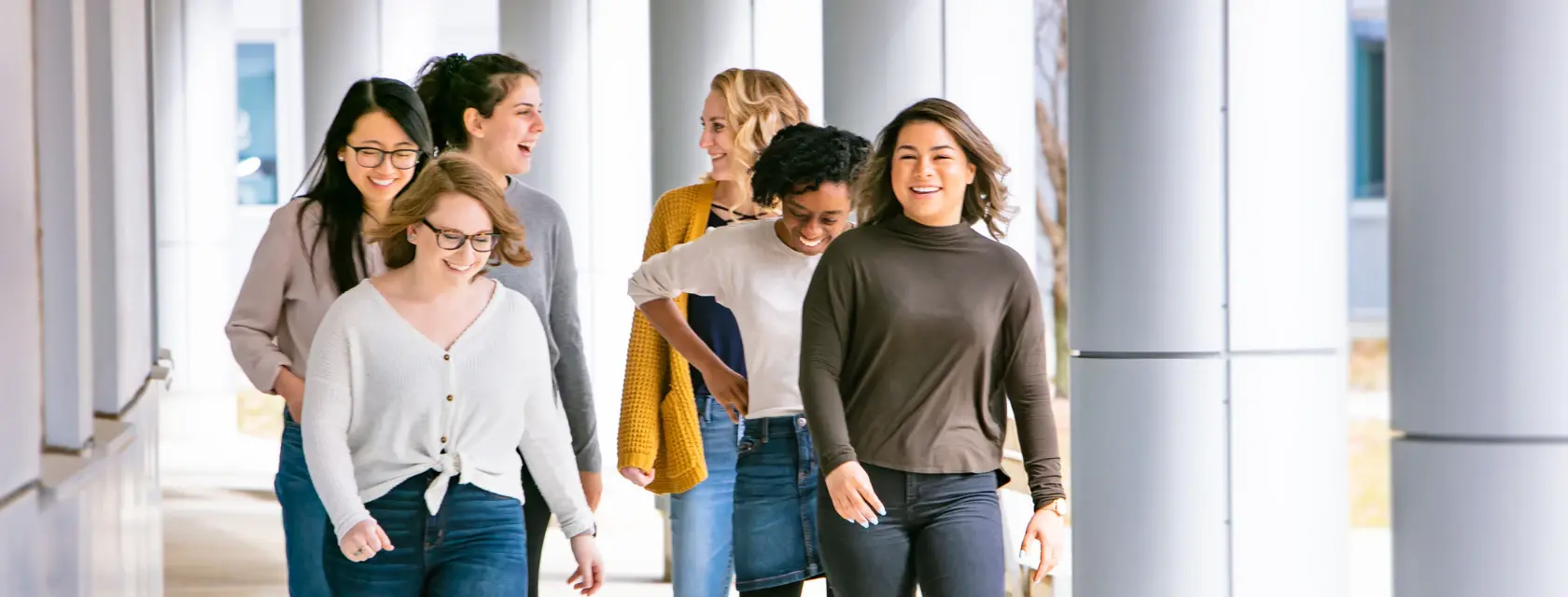 A group of six people are walking and smiling in a covered outdoor walkway.