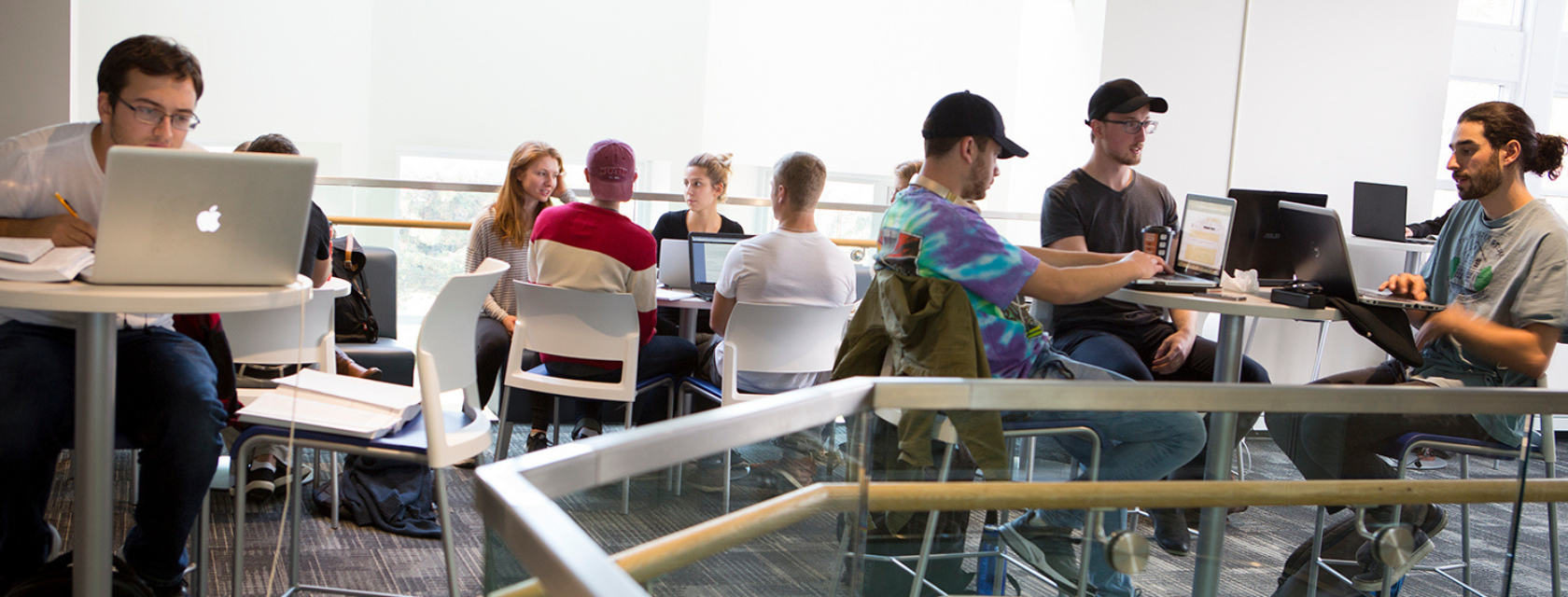 Students engaged in collaborative work on laptops within a modern classroom setting, focused on their tasks.