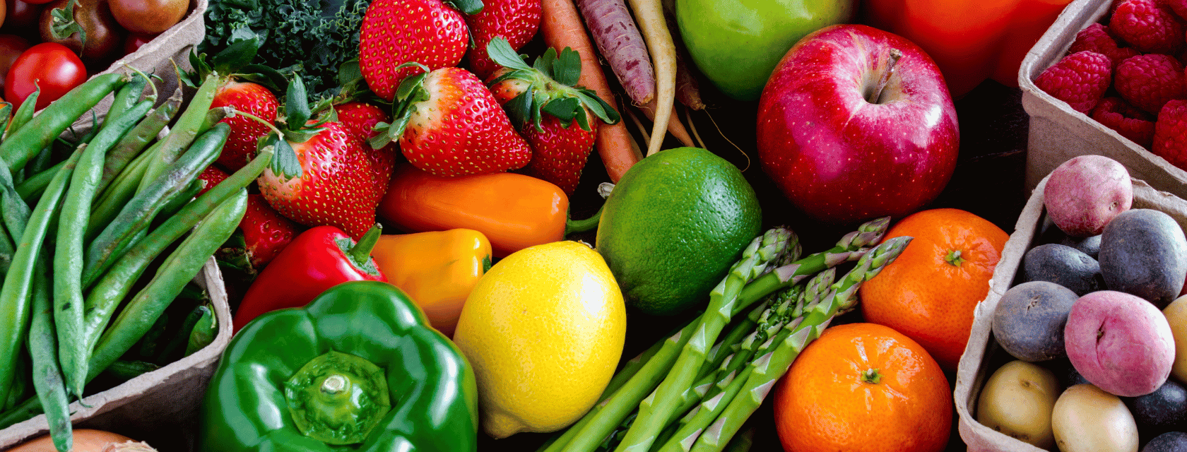 An assortment of fresh fruits and vegetables including strawberries, apples, green beans, peppers, lemons, limes, asparagus, raspberries, and peaches.