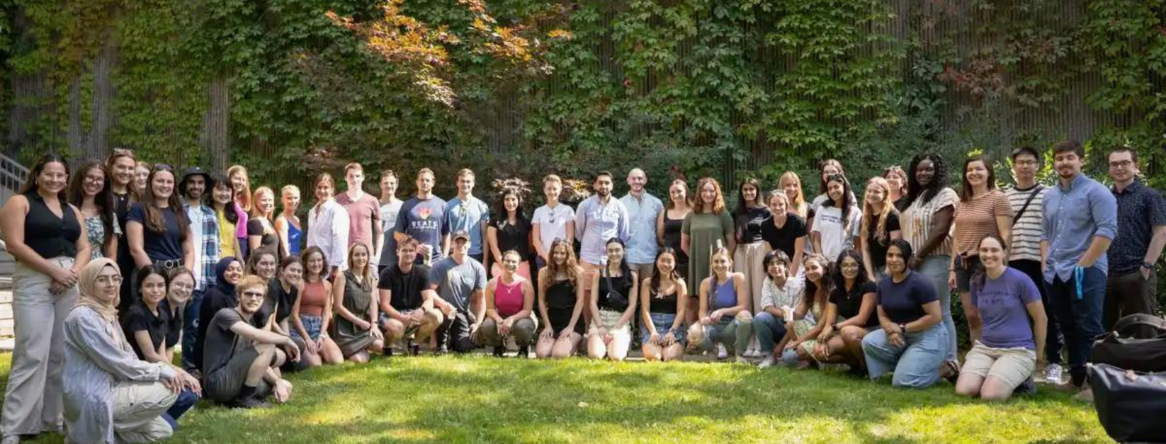 A diverse group of individuals seated in a circle on green grass, engaged in conversation and enjoying the outdoors.