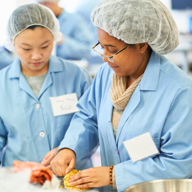 Two women wearing blue coats in a lab, and standing together.