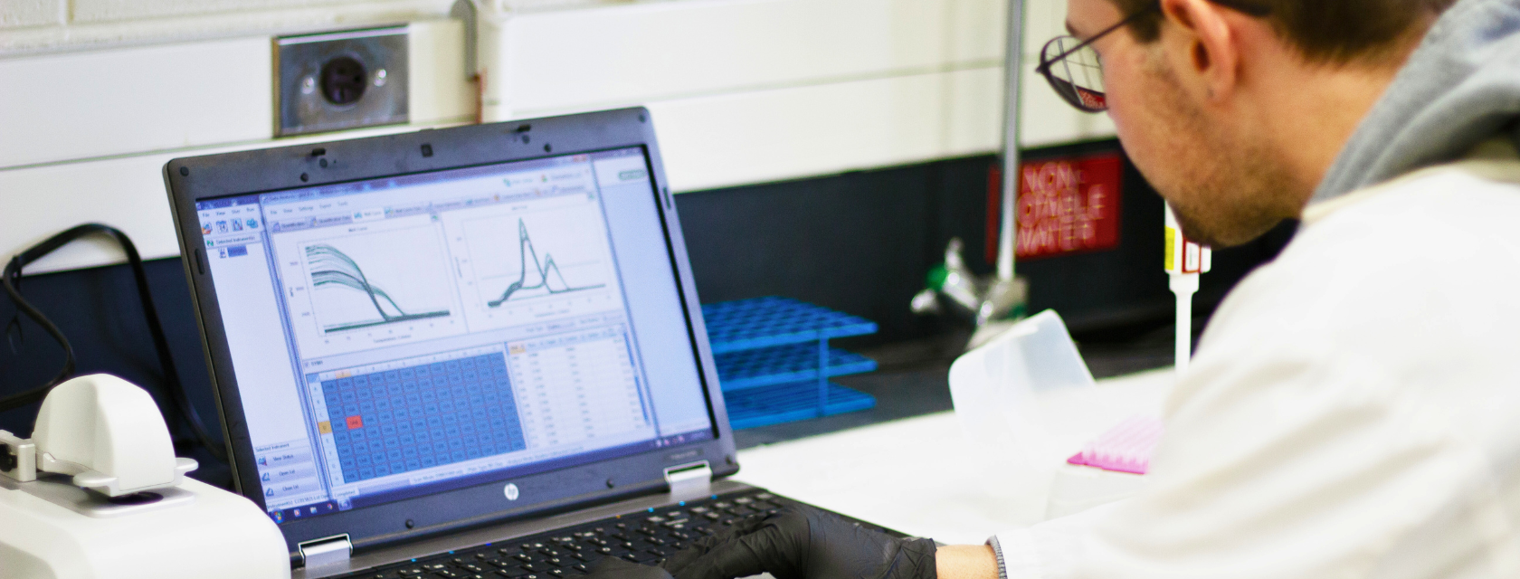 A student in a lab coat focused on his laptop, engaged in research and analysis in a lab.
