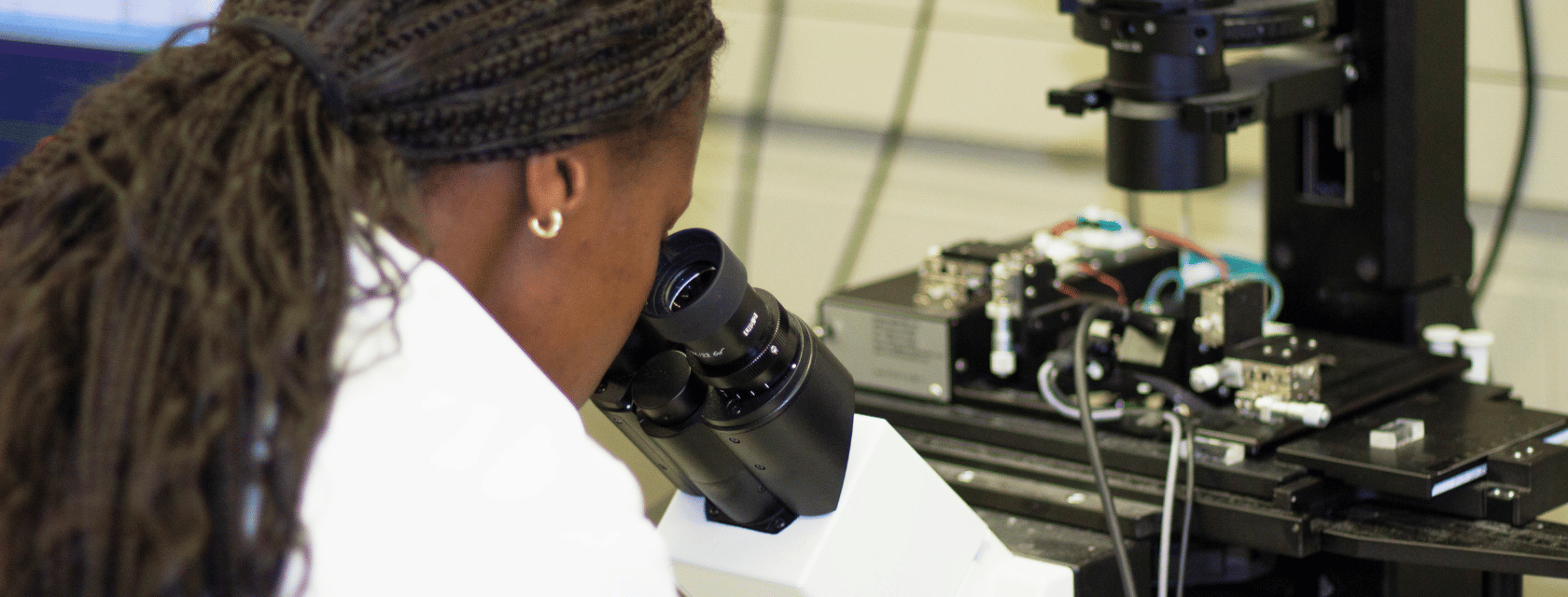 A female scientist in a white lab coat observes a sample through a microscope, focused on her research.