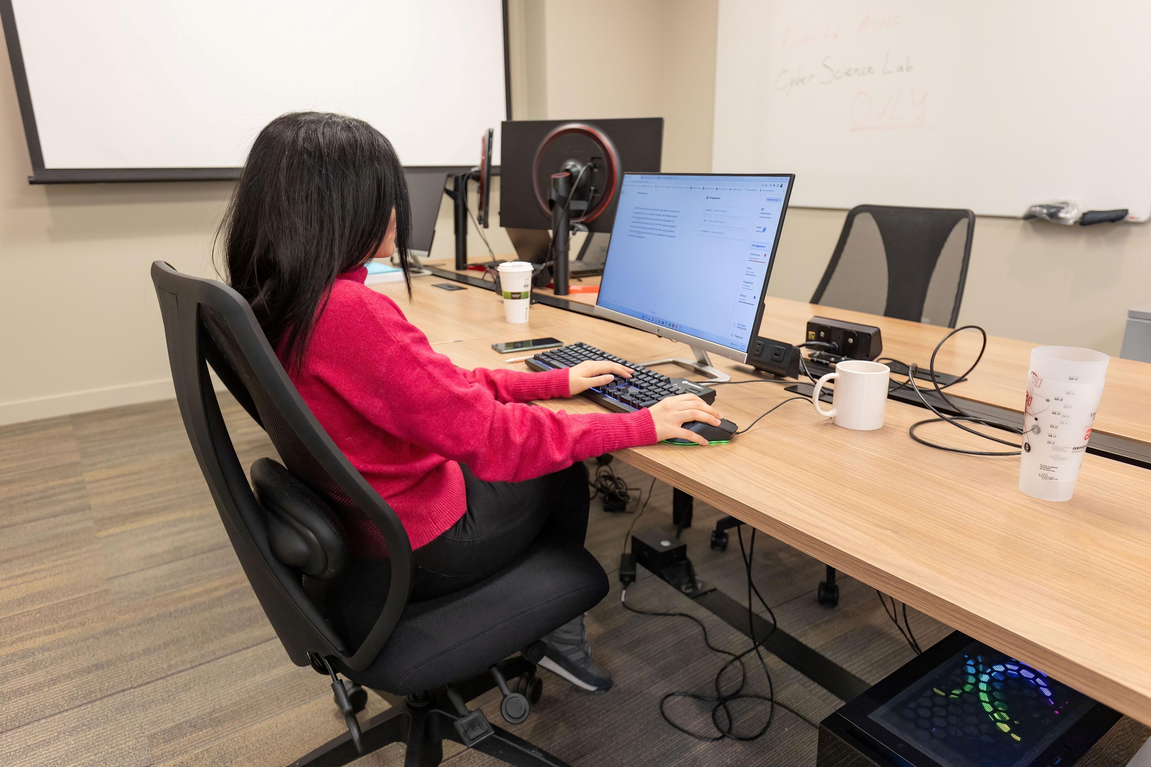 Student sitting in a classroom, studying on a monitor with whiteboards in the background.