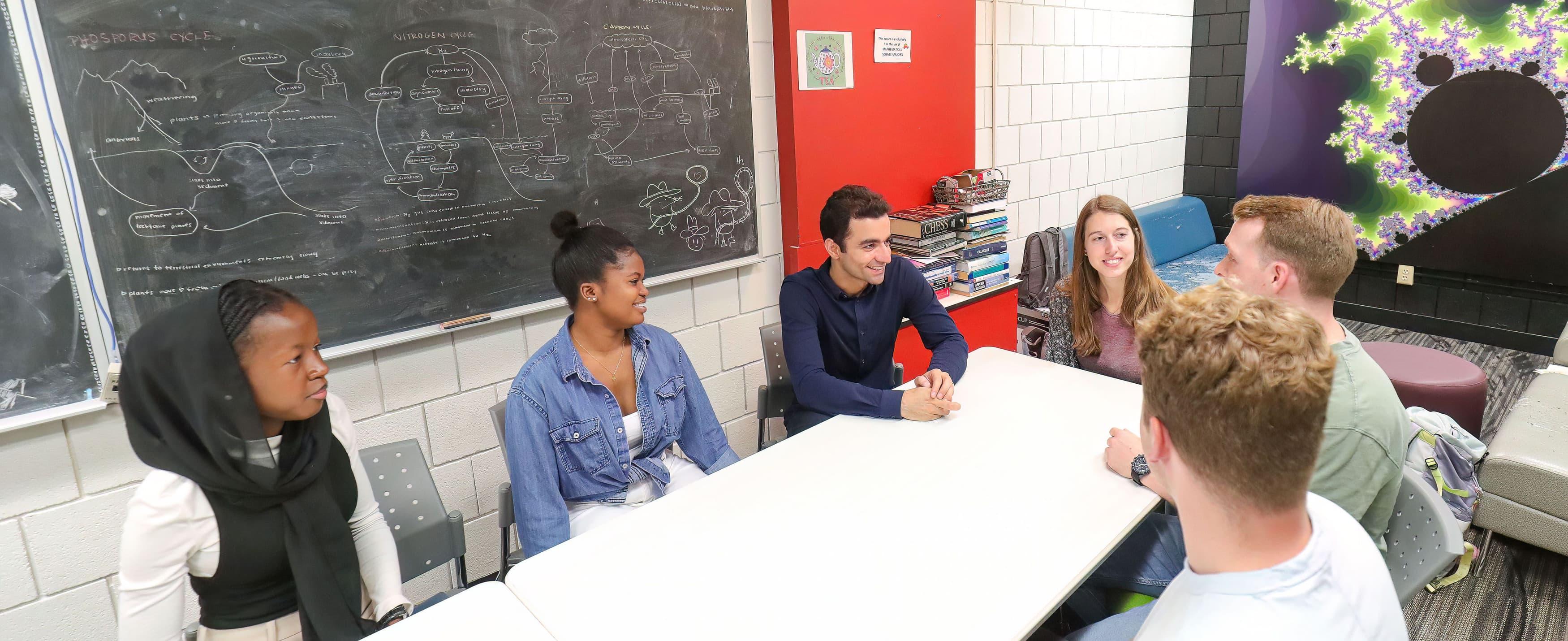 Group of math students sitting around a table and smiling in MacNaughton math study space