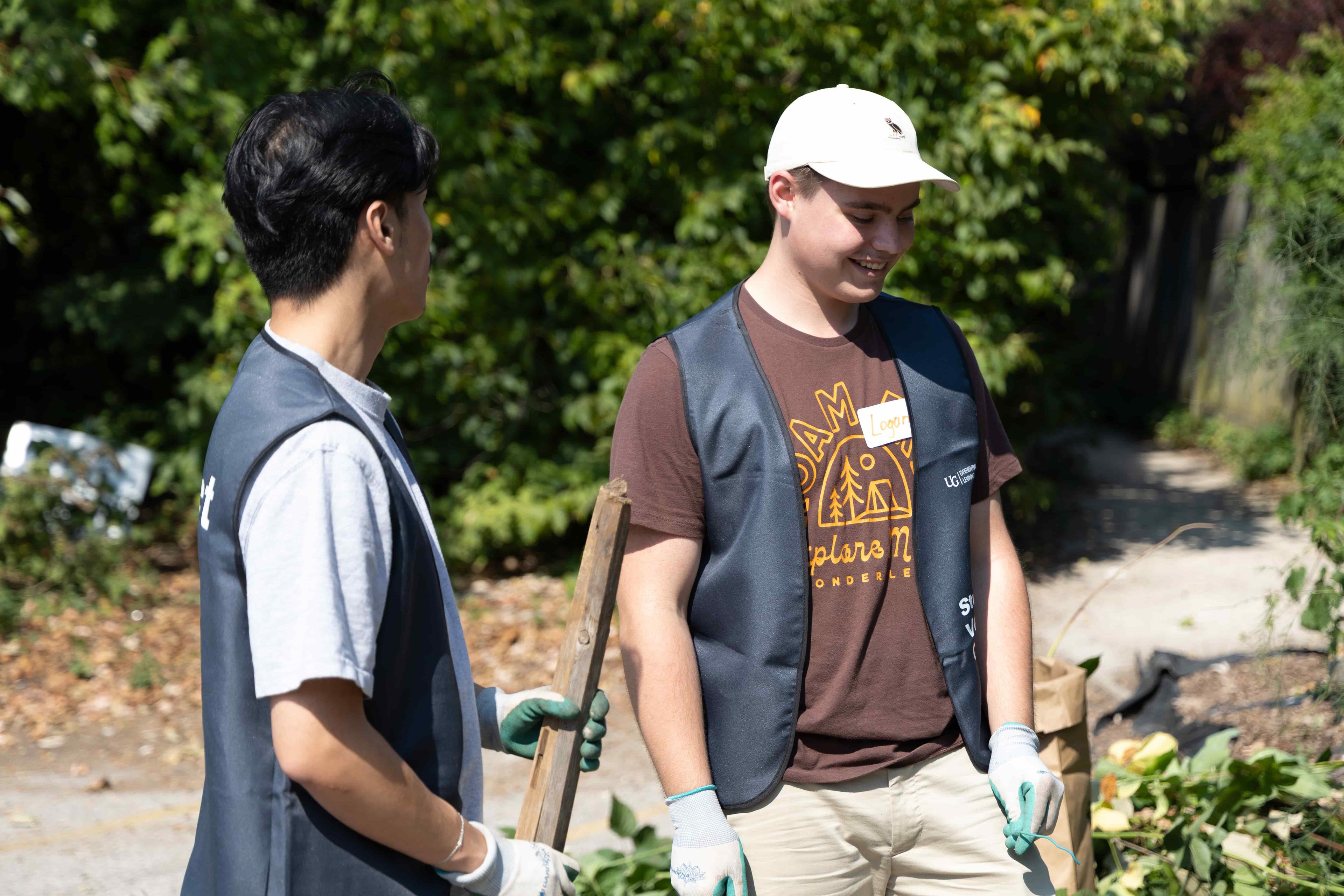 Two student volunteers smile while holding shovels near a garden.