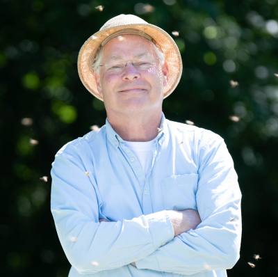 Paul Kelly stands proudly amongst a few flying honey bees