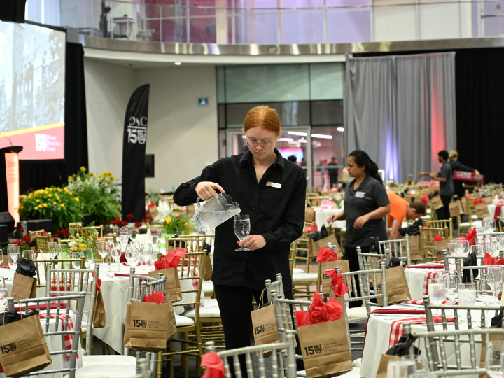 A Hospitality Services Catering staff members pouring water into a glass at an event.