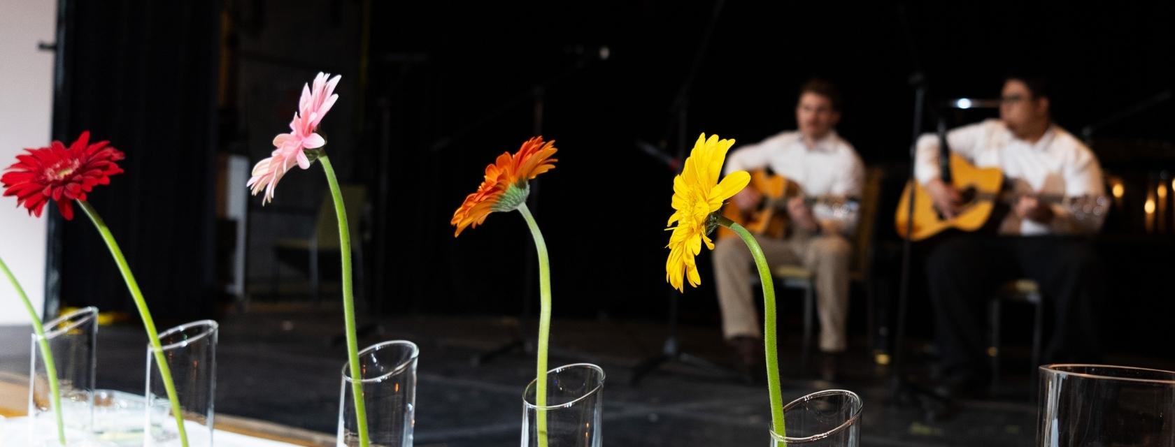 Daisies in vases in front of guitarists on a stage