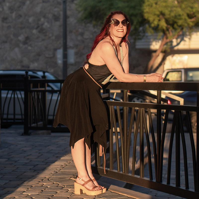 Woman in a black dress leaning against a railing.