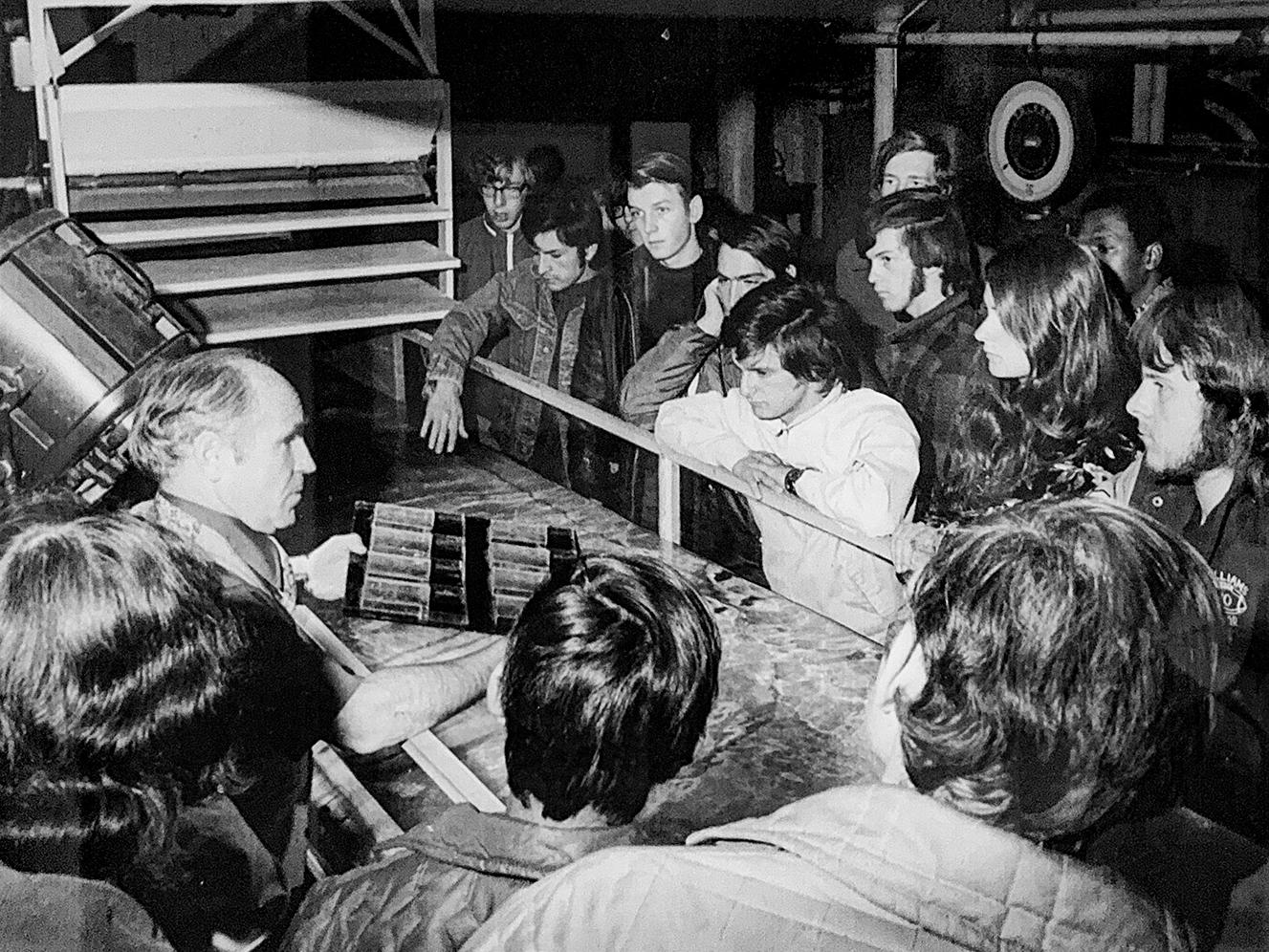 old black and white photo of a professor showing students something in a machine shop