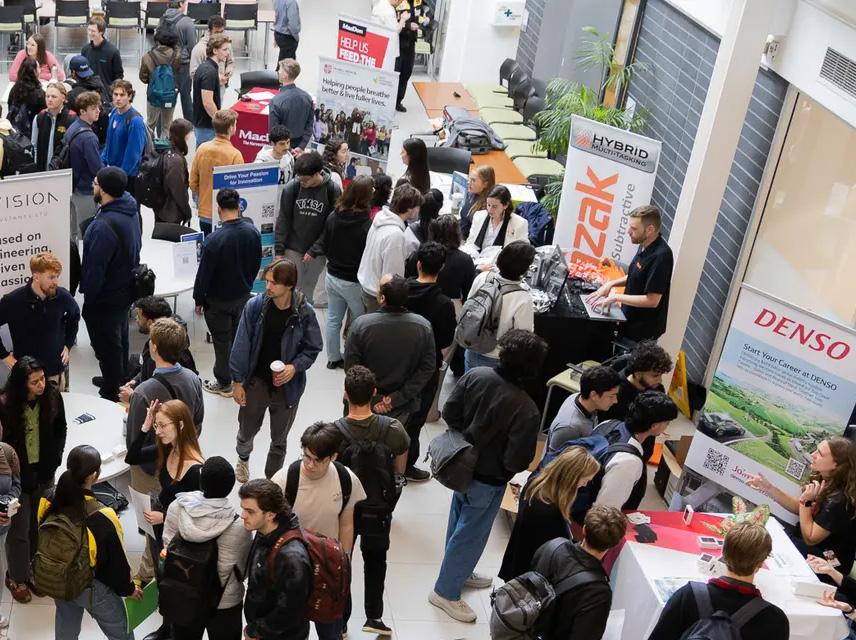 group of students in a large room surrounding company banners and booths