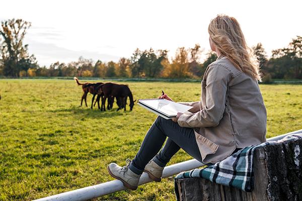 Girl with notepad watching horses in a field.