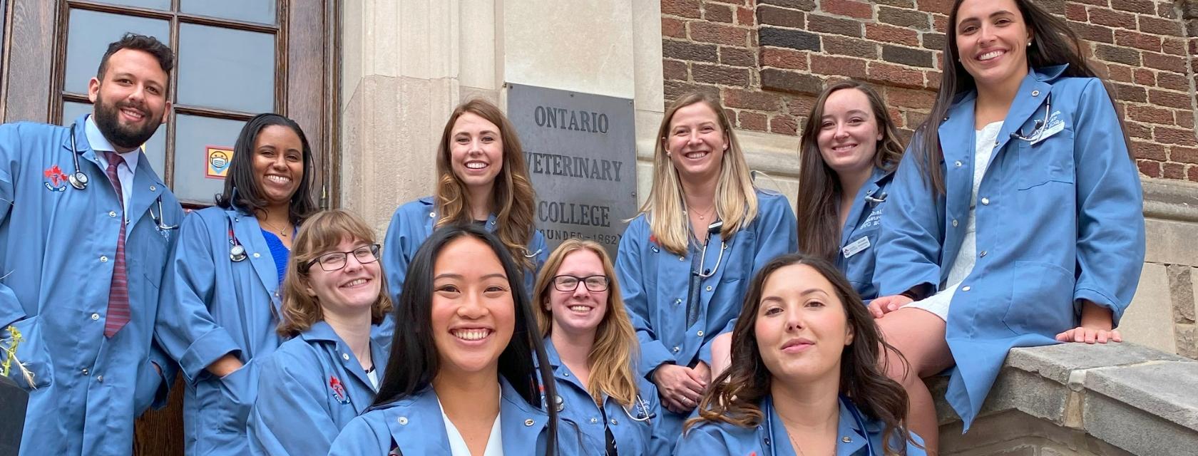A group of veterinary students wearing blue coats in front of a red brick building
