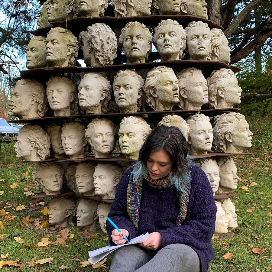 A woman sitting in the Donald Forster Sculpture Park in front of head sculptures