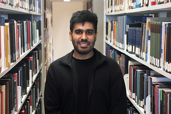 Young male student standing among bookshelves in the library.