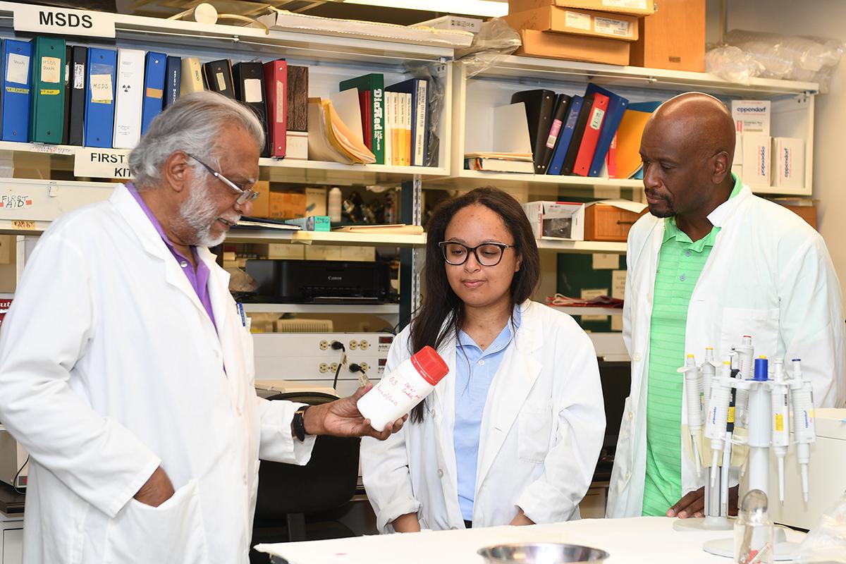 Three scientists in a lab holding an orange container