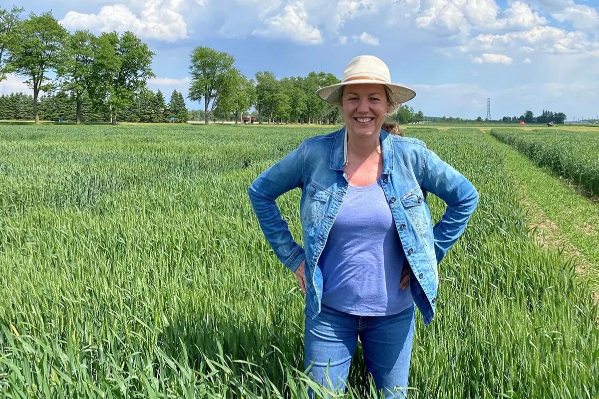 Booker stands in a field of knee-white, green (young) wheat, wearing casual clothes and a hat