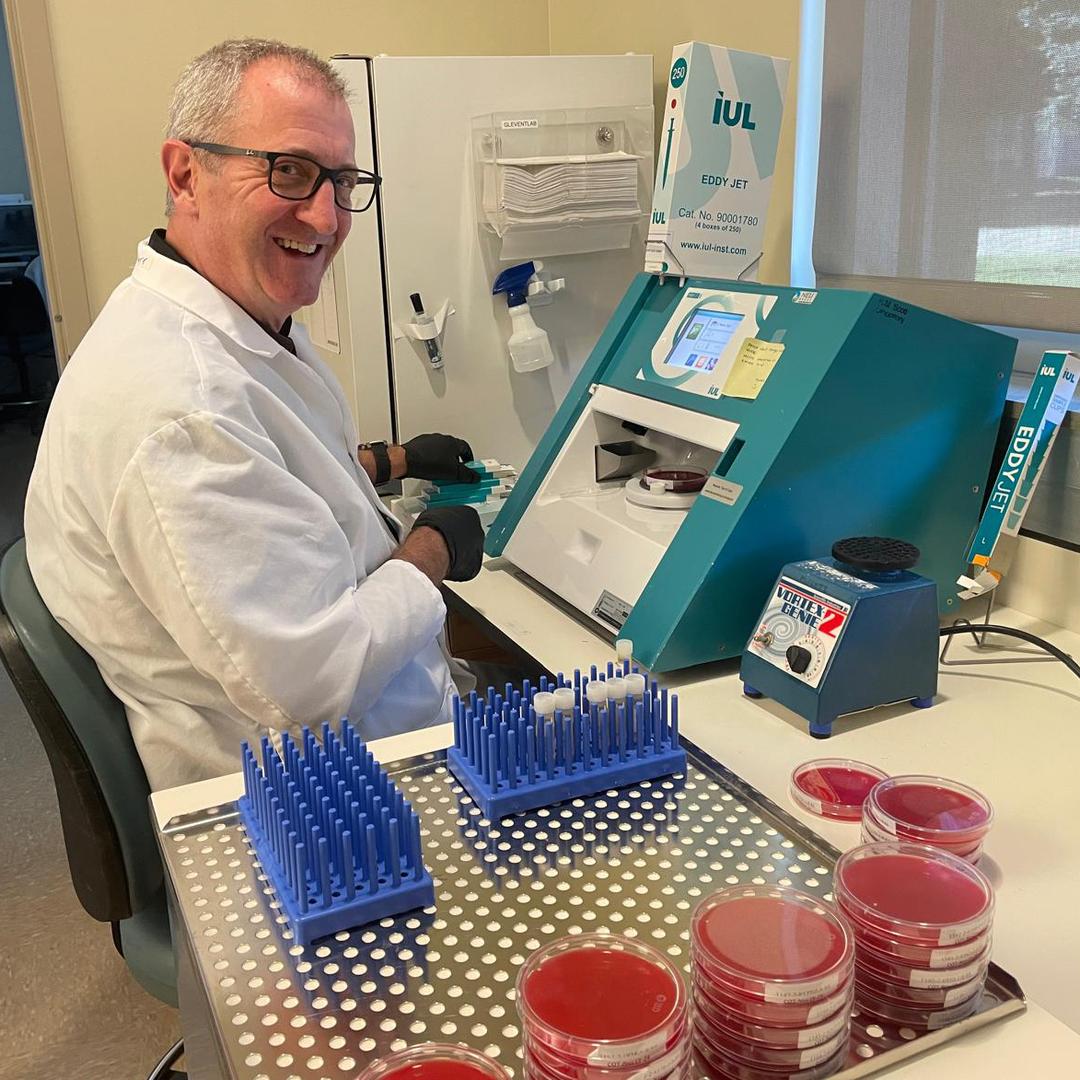 A man wearing a white lab coat and glasses working in a lab