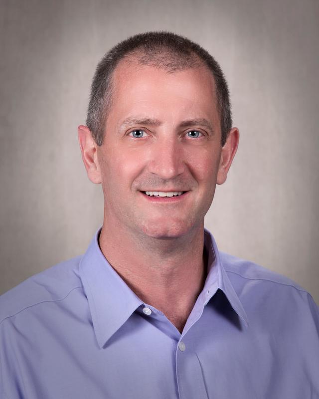 Headshot of a man wearing a blue shirt and smiling for the camera