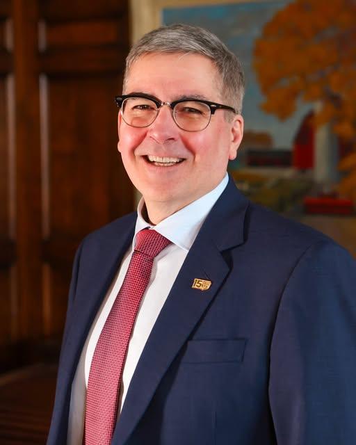 John Cranfield wearing a suit and tie, smiling to the camera