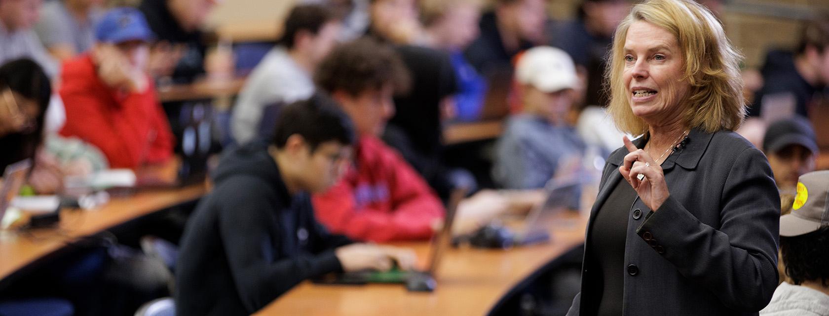 Female leader addressing students in a lecture hall.