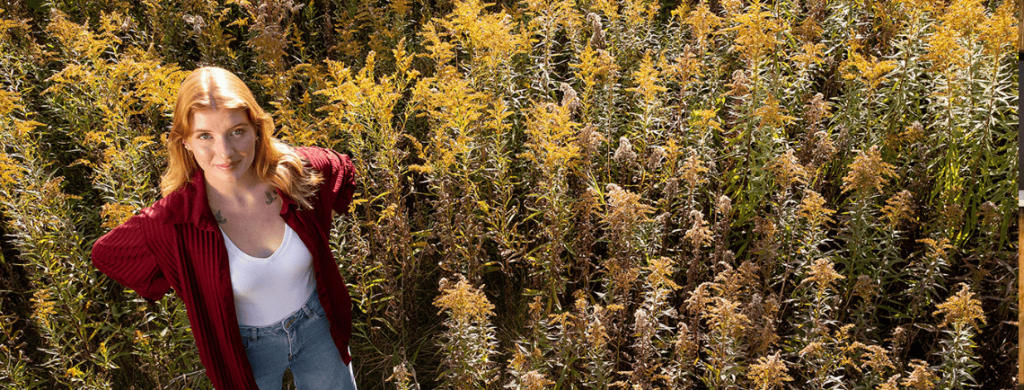 ava standing in a field with crops. she's wearing a red shirt on. the crops are yellow
