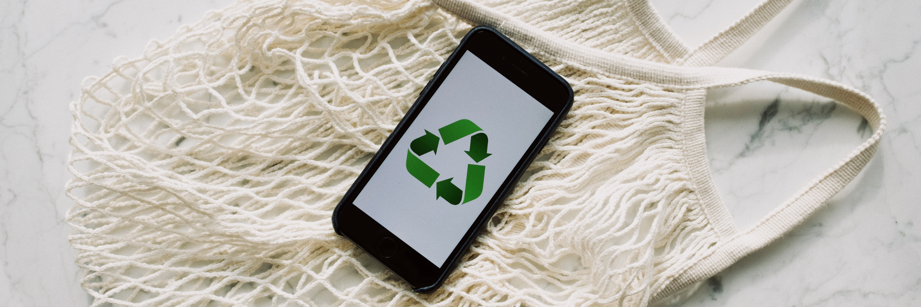 Recycling symbol on a phone, placed on top of a reusable shopping bad
