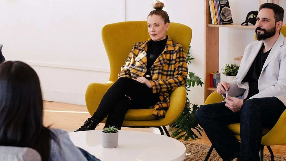 Two people each sitting in a chair appearing to be listening.