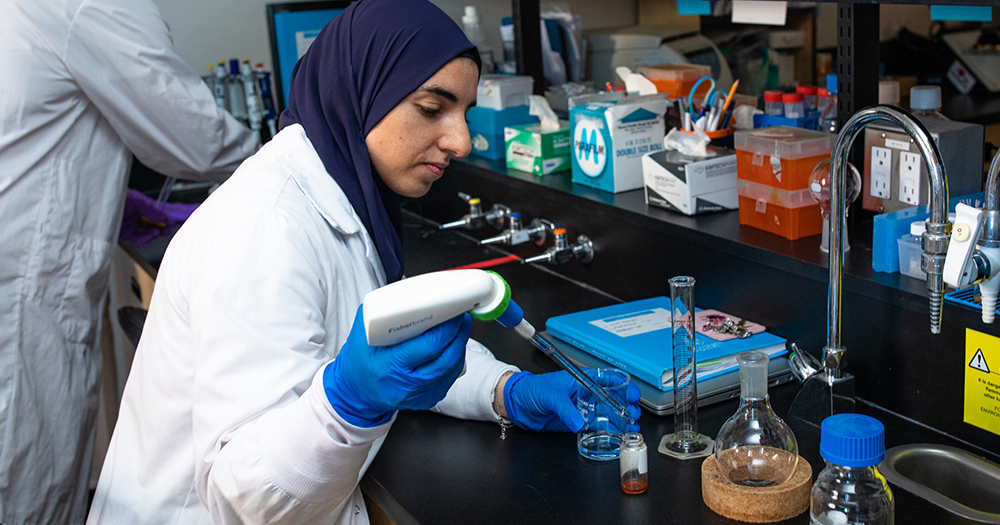 student holding a testing device, analyzing a specimen, wearing a labcoat
