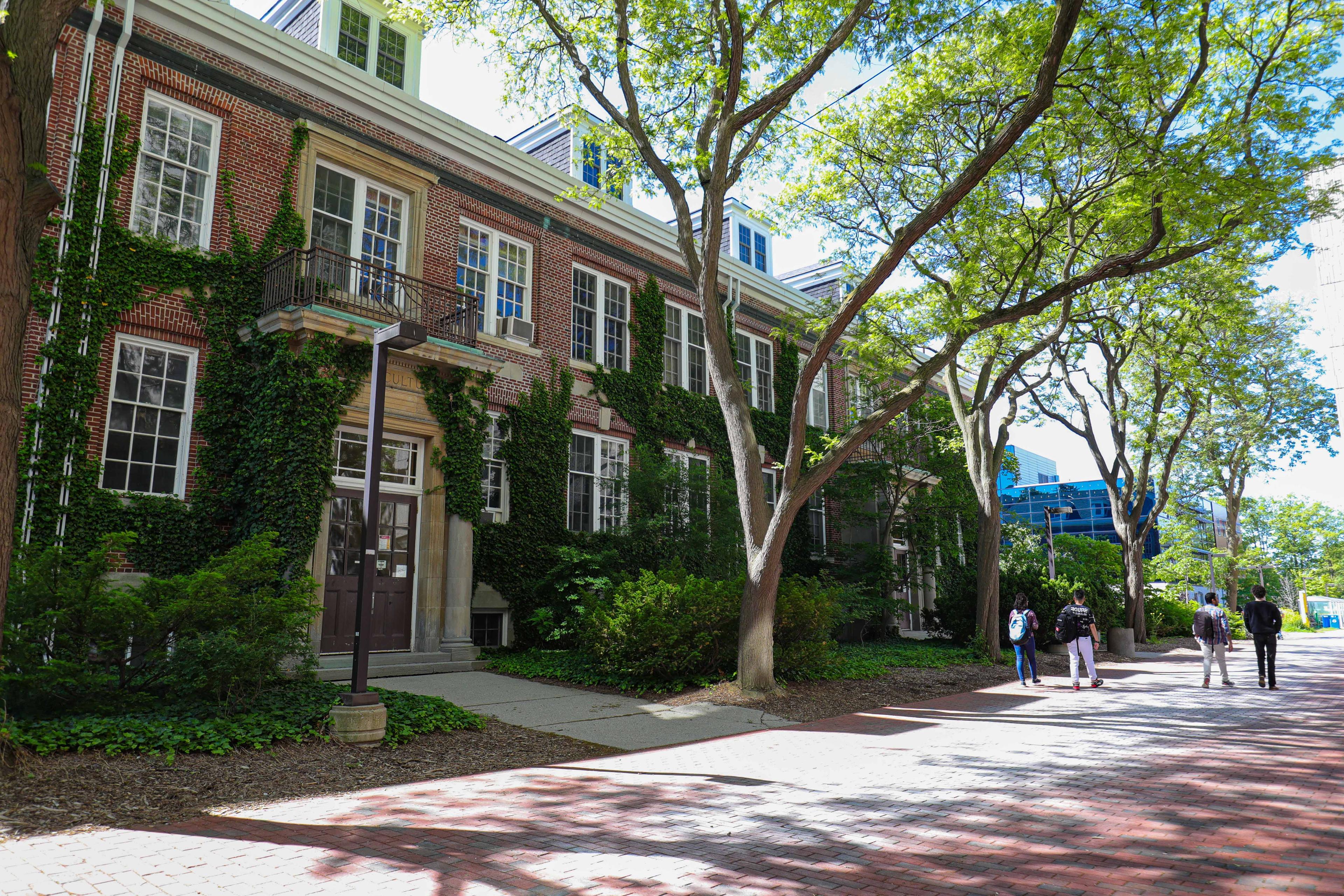 3 students walking on a brick walkway in front of a red building