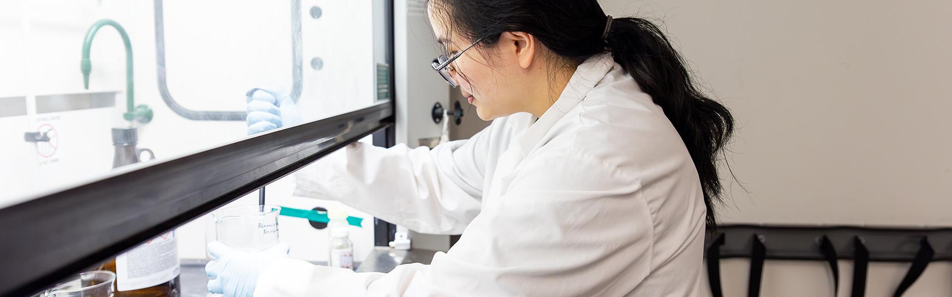Female student in a lab, pipetting a solution from a beaker